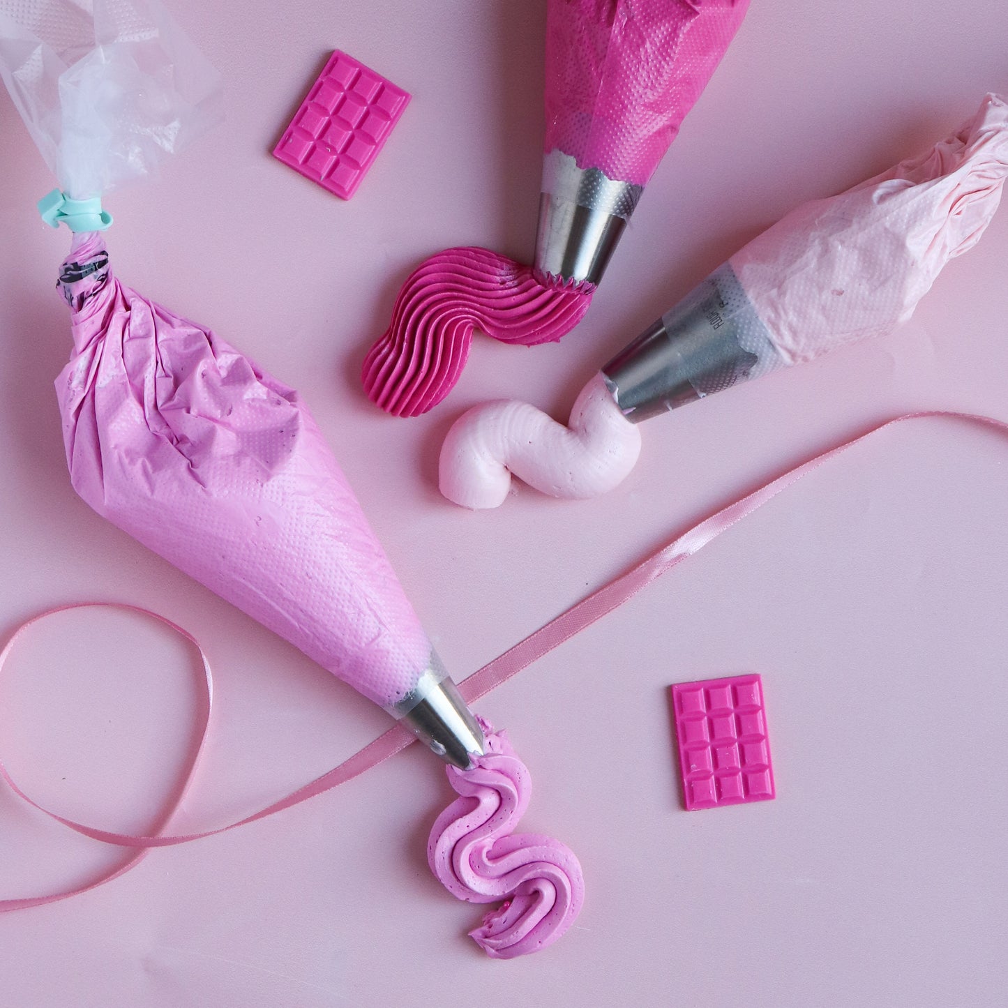 Pink frosting piping bags and decorations on a pink background